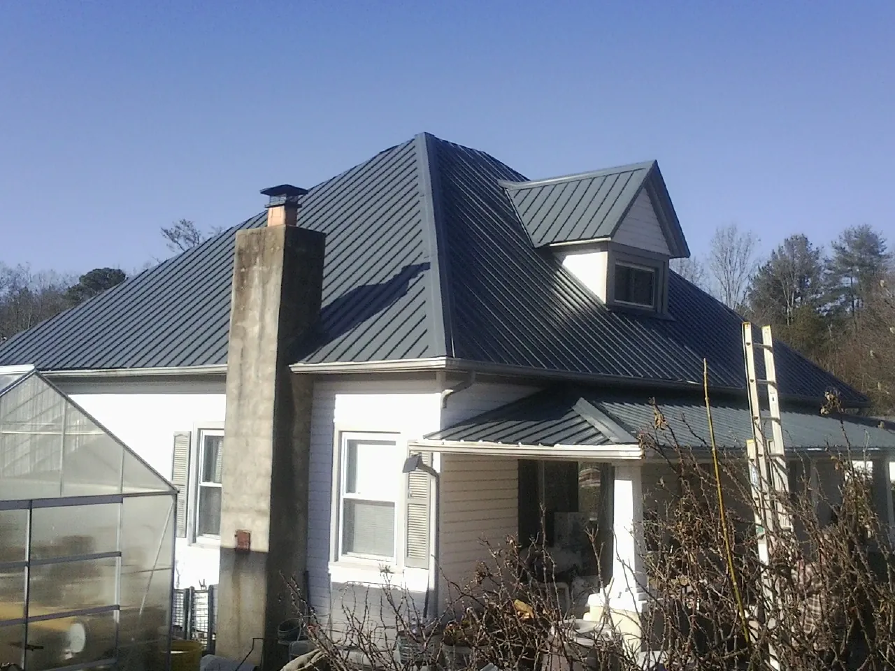 Dark blue standing seam metal roof on a white farmhouse with dormer — Slate & Tile Roof Repair by Roofing Brothers in Tumtum
