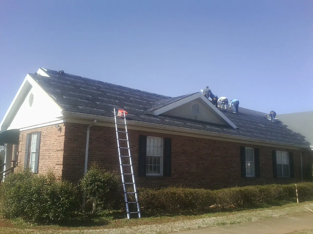 Crew tearing shingles off a brick ranch roof with a ladder set — Emergency Roof Repair work by our crew in Tumtum