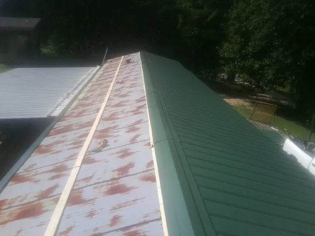 Old rusted panels beside newly installed green metal roofing — Wind Damage Roof Repair by Roofing Brothers in Tumtum