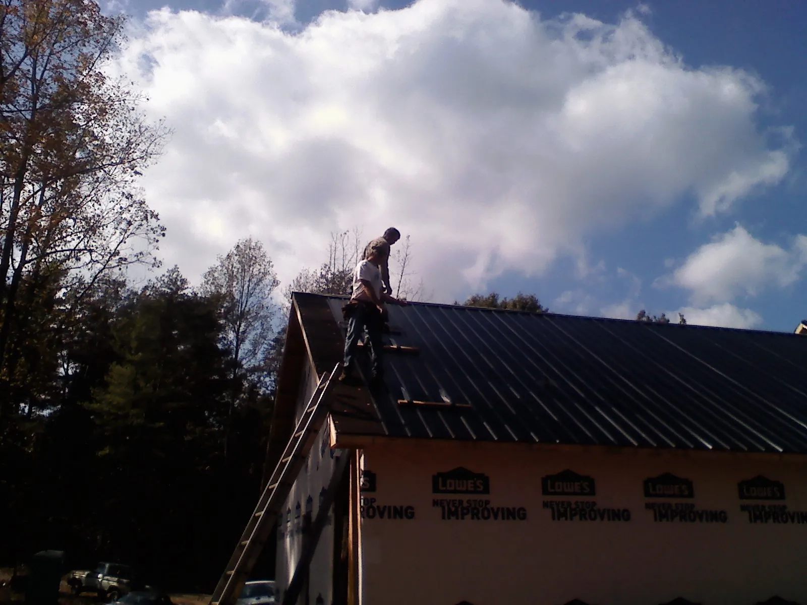 Roofer fastening dark metal panels high against a cloudy sky, from a Roof Inspection job in Tumtum
