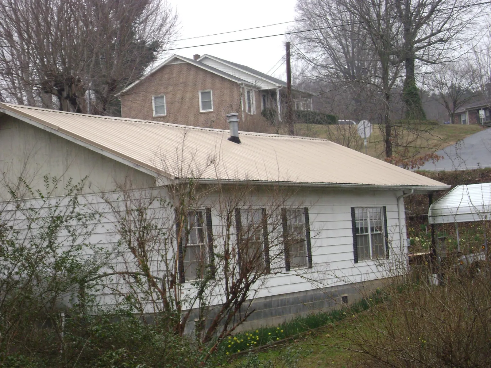 Tan metal roof on a white sided house set into a hillside — Commercial Roofing by Roofing Brothers in Tumtum