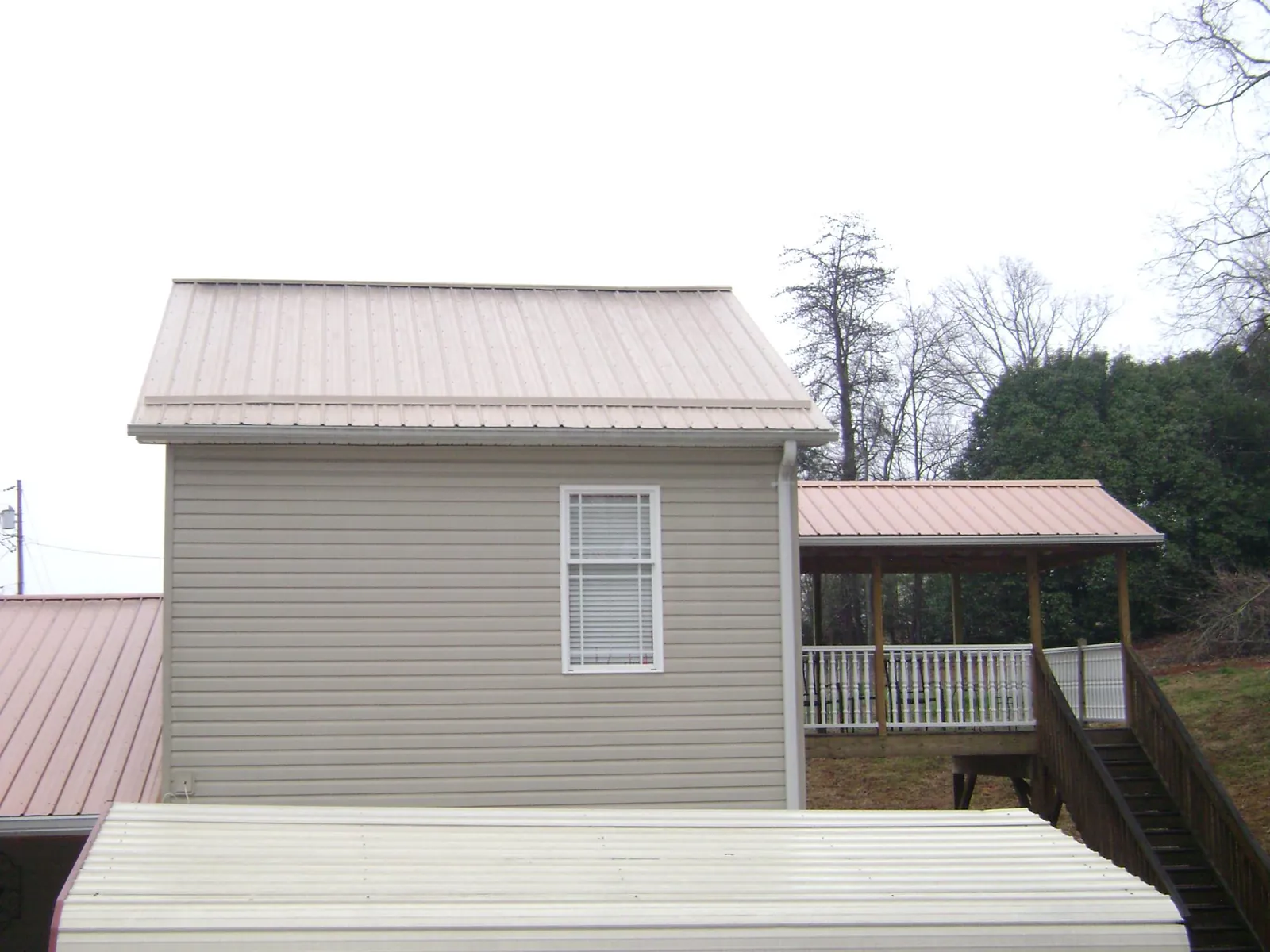 Tan metal roofs on a two story addition and attached porch, from a Roof Replacement job in Tumtum